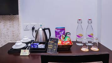 A hotel room's breakfast table with a kettle, tea set, snacks, a menu, and bottled water.
