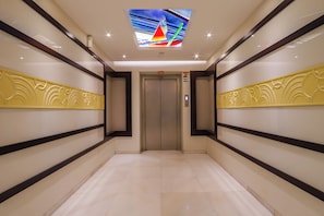 A modern elevator with a digital display, a clean hallway with patterned walls, and a tiled floor. - Hotel Godwin Deluxe Near New Delhi Railway Station (New Delhi)