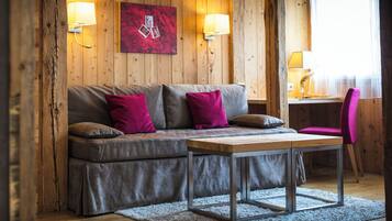 Une pièce chaleureuse avec un mur en bois, un canapé gris agrémenté de coussins rouges, une table en bois et une chaise rose.
