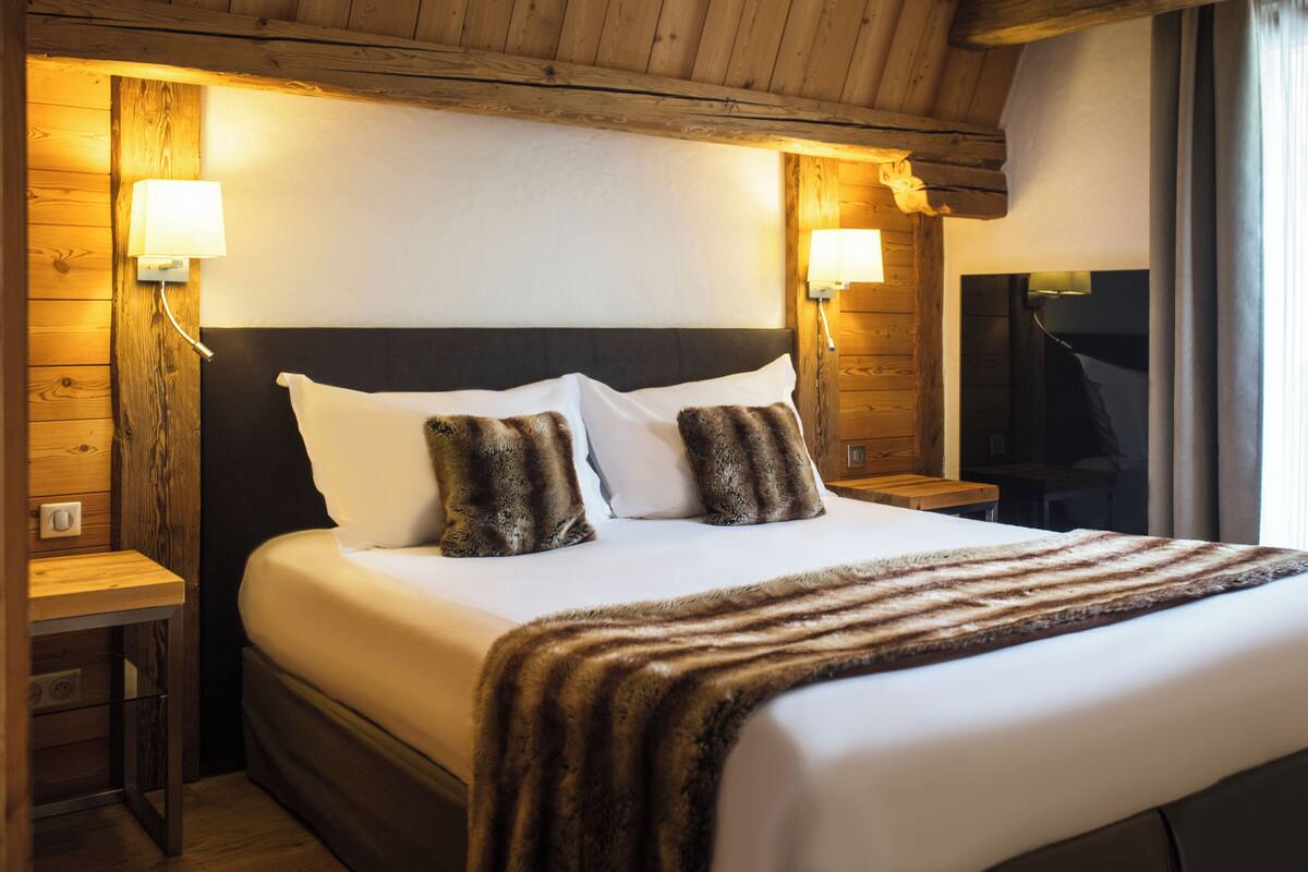 A hotel room with a large bed, wooden headboard, two bedside tables, and wall-mounted lamps.