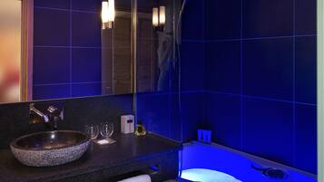 Une salle de bain moderne avec un grand lavabo, un miroir et une baignoire éclairée de lumière bleue.