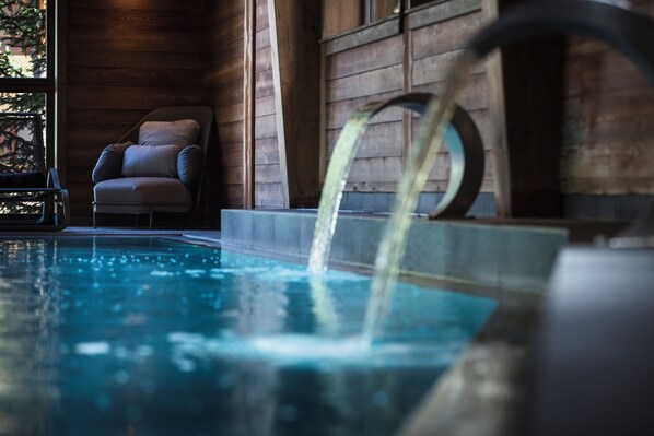 A pool area with a chair and a water feature. - Au Coeur du Village (La Clusaz)