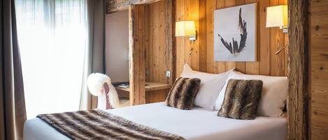 A hotel room with a wooden paneled wall, a bed with white linens, two wall-mounted lamps, and a framed artwork above the bed.