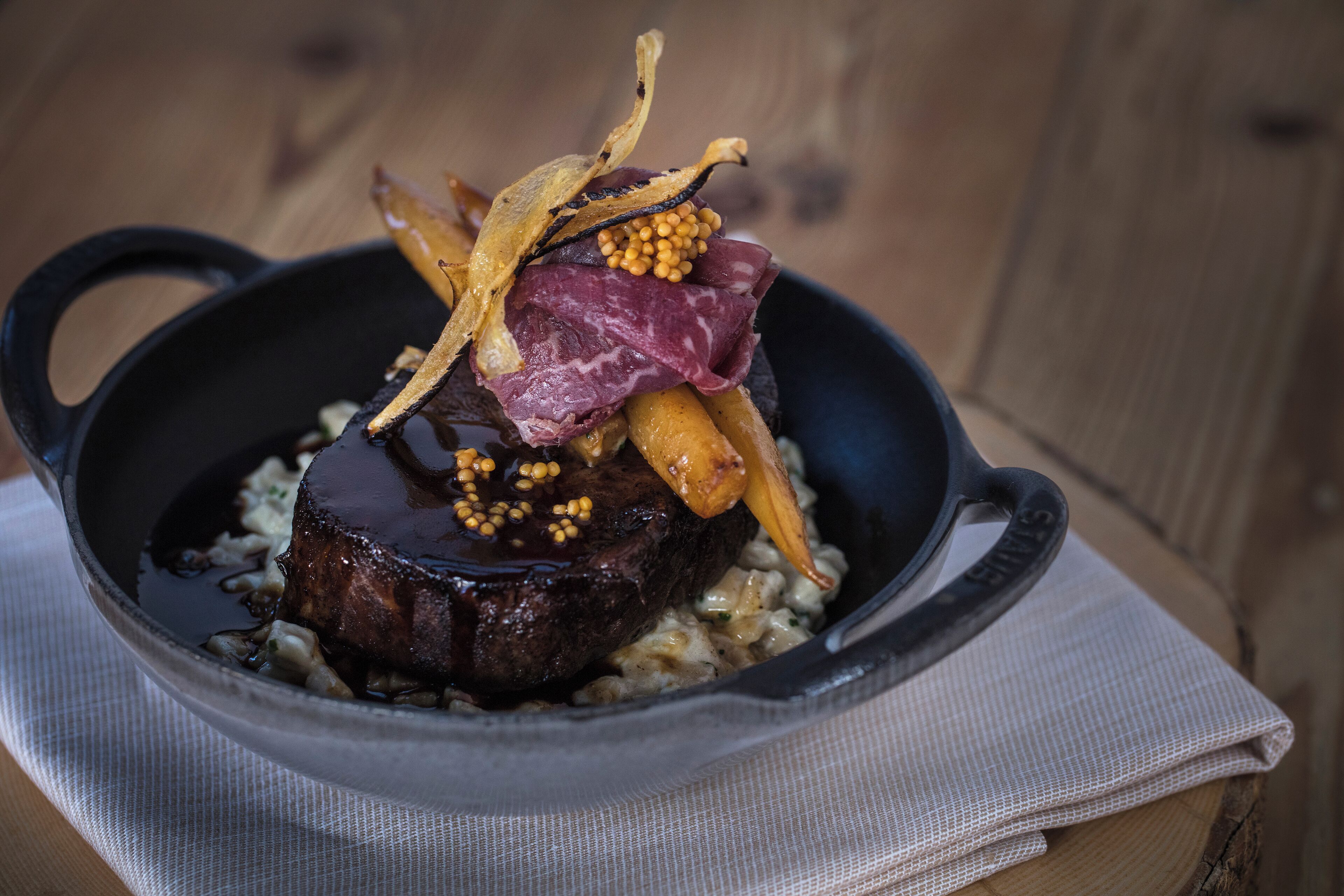 A steak with garnish in a cast iron skillet on a wooden table.