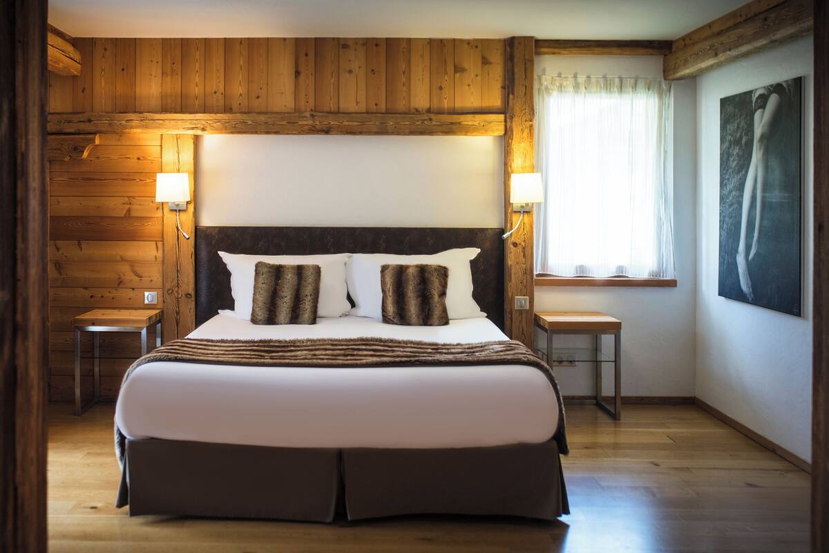 A bedroom with a large bed, wooden walls, a window with curtains, and a painting on the wall.