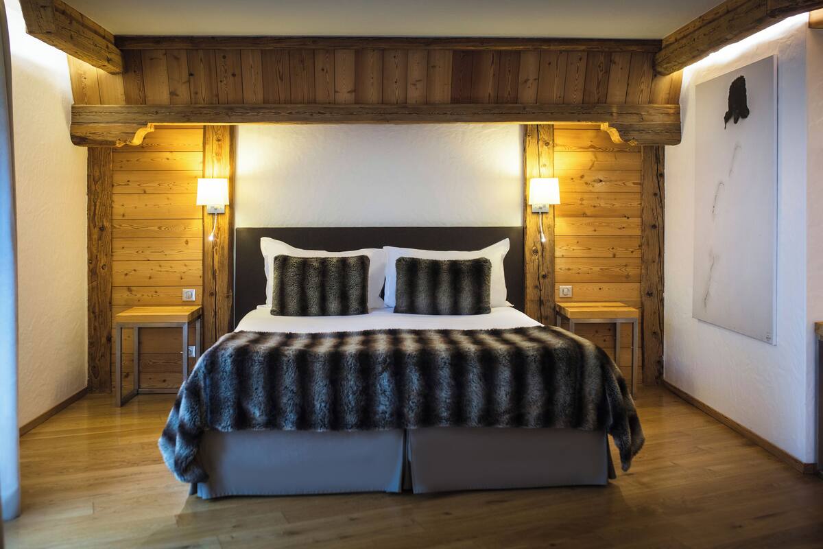 A bedroom with a wooden ceiling, a large bed with two pillows, two bedside tables, and two wall-mounted lamps.