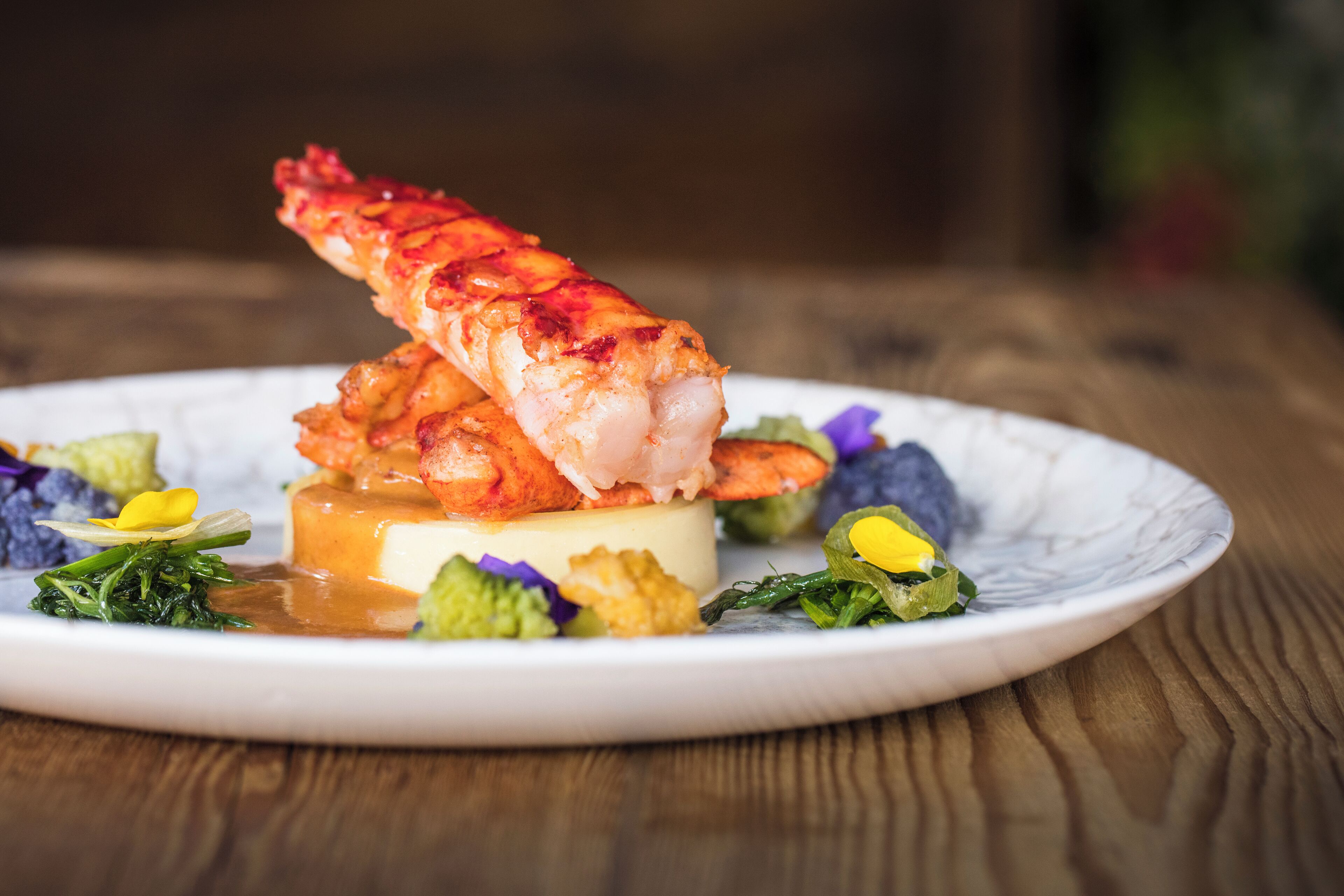 Une assiette comprenant une queue de homard, une sauce crémeuse et quelques légumes verts.