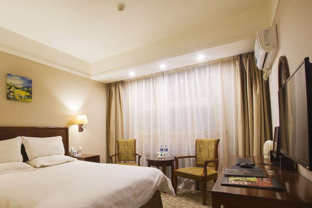 A hotel room with a large bed, two chairs, a desk with a computer, a TV, and a window with curtains.