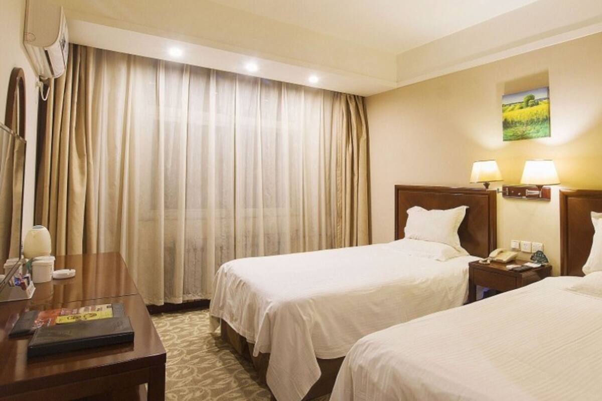 A hotel room with two beds, a desk, a lamp, and a painting on the wall.