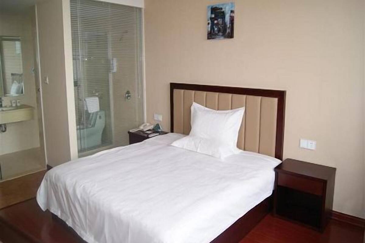A hotel room with a bed, a bedside table, a nightstand, a mirror, and a bathroom with a shower and toilet.