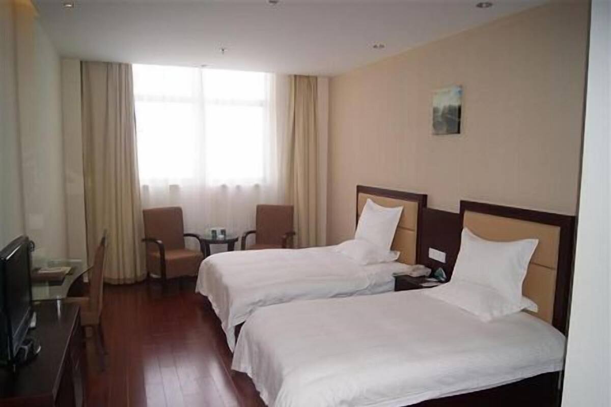 A hotel room with two single beds, a desk with a chair, a television, and a window with curtains.