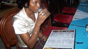 A person seated at a table with a menu, a glass, and a bottle. - Hotel Azur (Yaoundé)