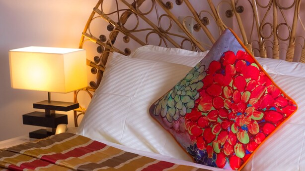A bed with a patterned bedspread, a decorative pillow, a bedside lamp, and a metal headboard. - Hotel Azur (Yaoundé)