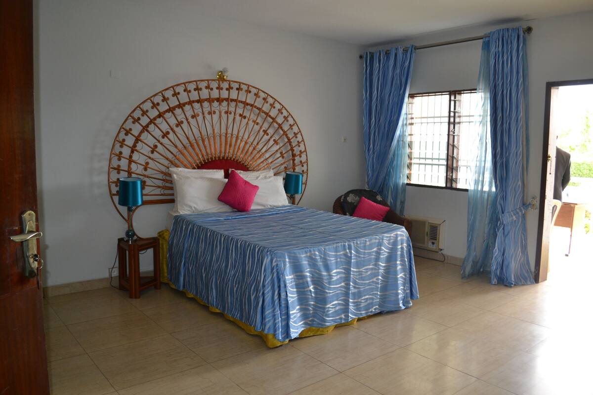 A bedroom with a bed, a round headboard, a window with curtains, and a door.
