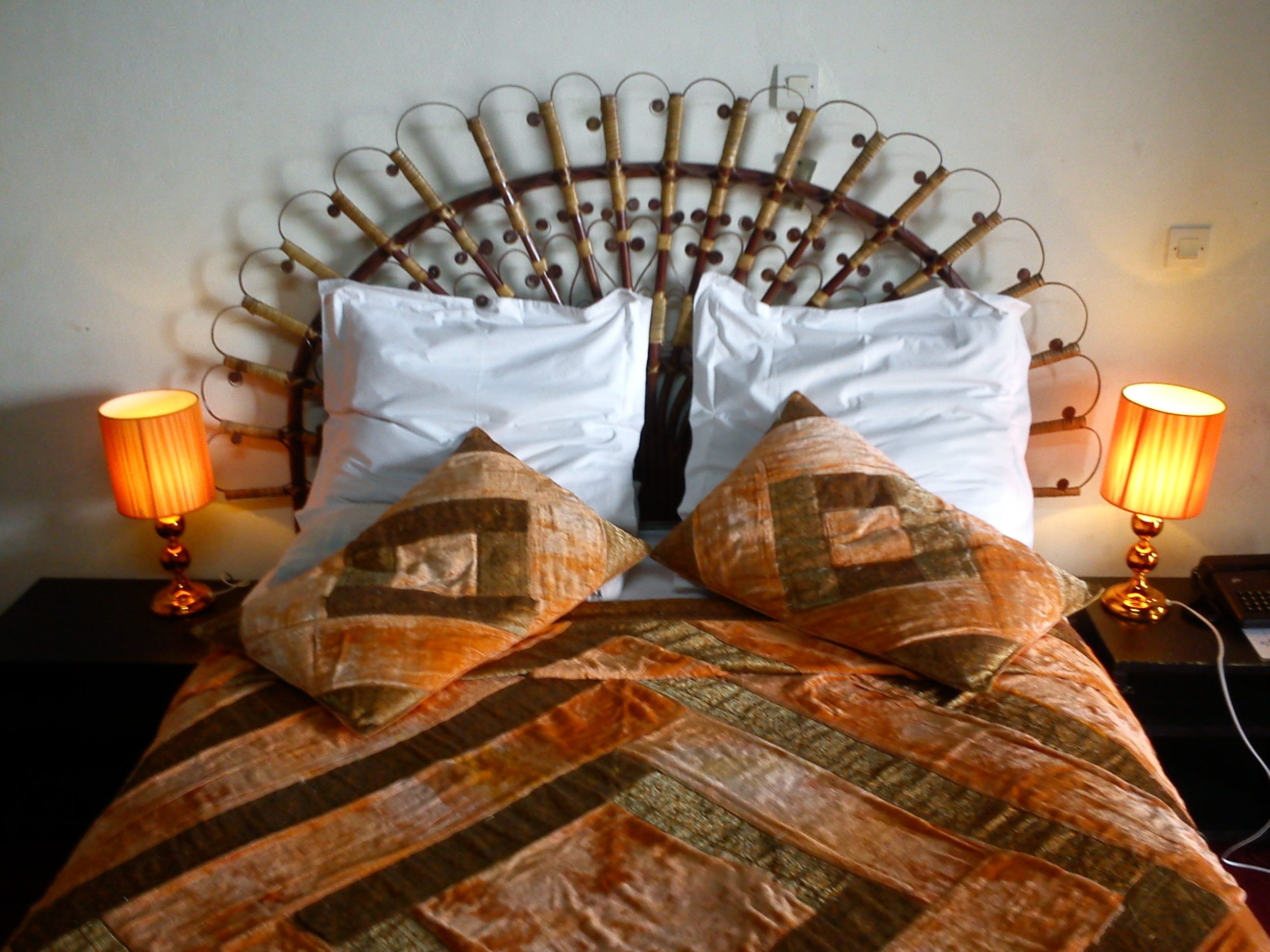 A bed with a metal headboard, two white pillows, and two patterned pillows. There are two bedside lamps on either side of the bed.