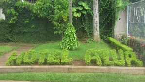 A garden with a pathway leading to a building with the sign "HOTEL AURA". - Hotel Azur (Yaoundé)