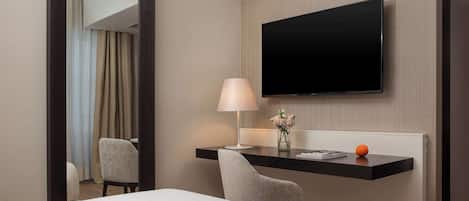 A hotel room with a bed, a desk with a lamp, a flat-screen TV, and a mirror.