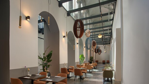 A modern restaurant interior with high ceilings, arched windows, and a long dining area with tables and chairs. - NH Collection Palermo Palazzo Sitano (Palermo)