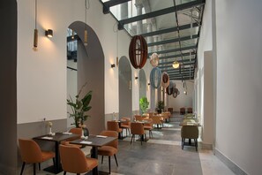 Un interior de restaurante moderno con techos altos, ventanas en arco y una amplia zona de comedor con mesas y sillas.