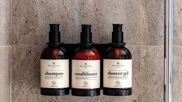 Three bottles of TH COLLECTION hotels shampoo, conditioner, and shower gel against a textured wall.