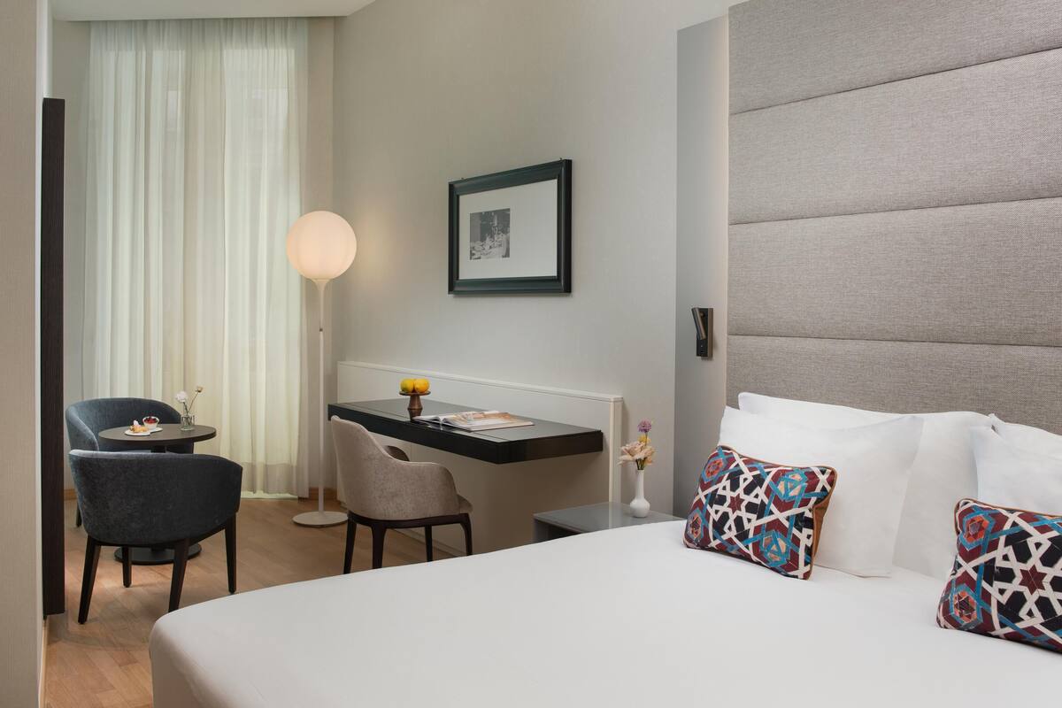 A hotel room with a bed, a desk, two chairs, a lamp, and a framed picture on the wall.