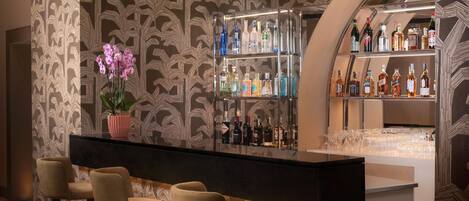 Zona de bar con papel tapiz estampado, una orquídea en maceta y una variedad de botellas de licores.