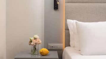 Une chambre d’hôtel moderne avec une table de chevet, un vase de fleurs, un citron et un luminaire fixé au mur.