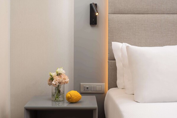 Una habitación de hotel moderna con una mesita de noche, un florero con flores, un limón y una lámpara de pared.