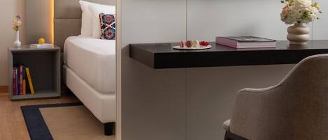 A modern hotel room with a bed, bedside table, TV, and a desk with a chair.