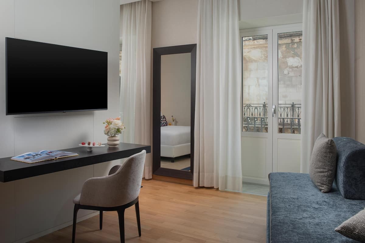A modern living room with a flat-screen TV, a dining area with a chair and a table, a sofa, and a balcony with a railing.