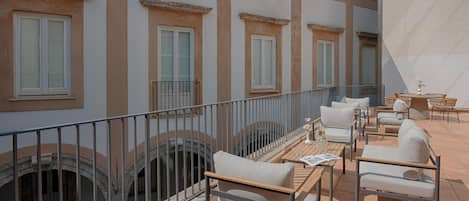 A terrace with outdoor seating, a railing, and a view of the building's architecture.