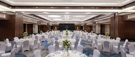 Un salón de banquetes con mesas redondas dispuestas para un evento formal, con un arreglo floral central.