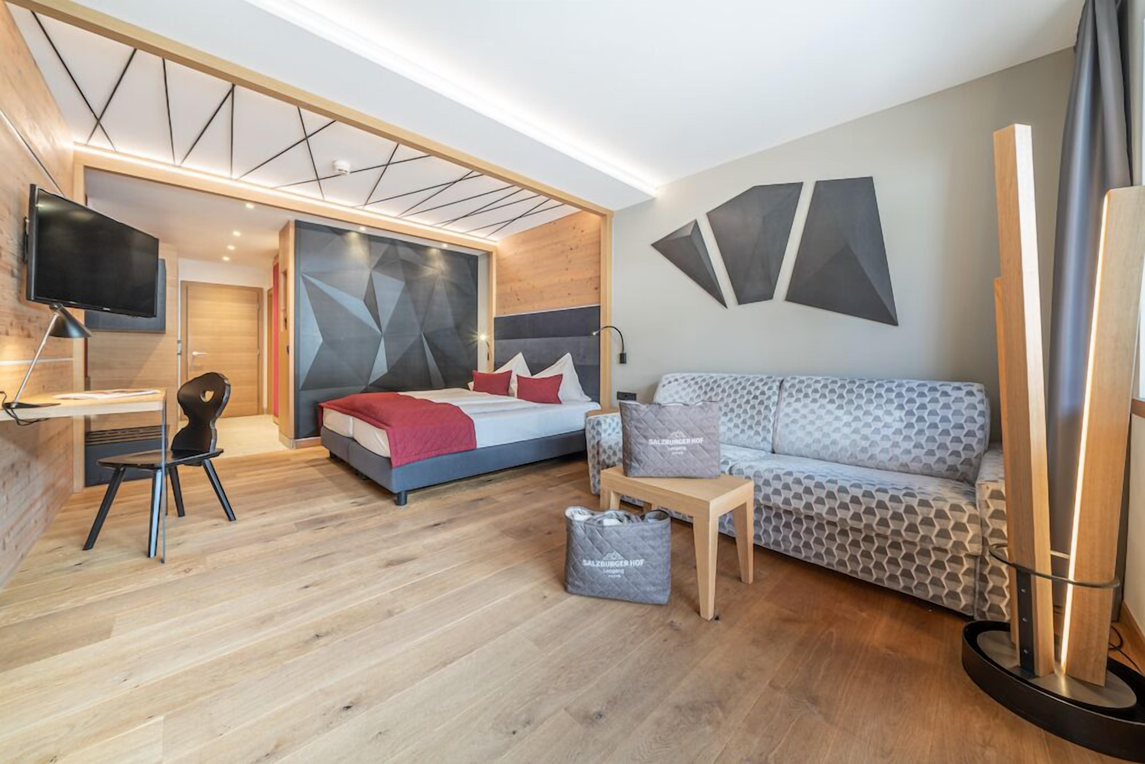 A modern hotel room with a bed, a sofa, a desk, and a TV.