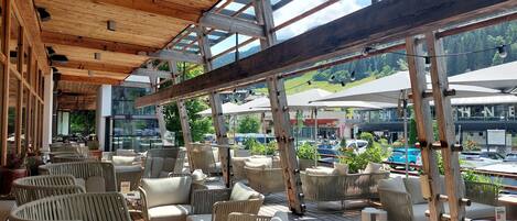 An outdoor seating area with wicker furniture and a wooden deck, overlooking a parking lot and buildings.