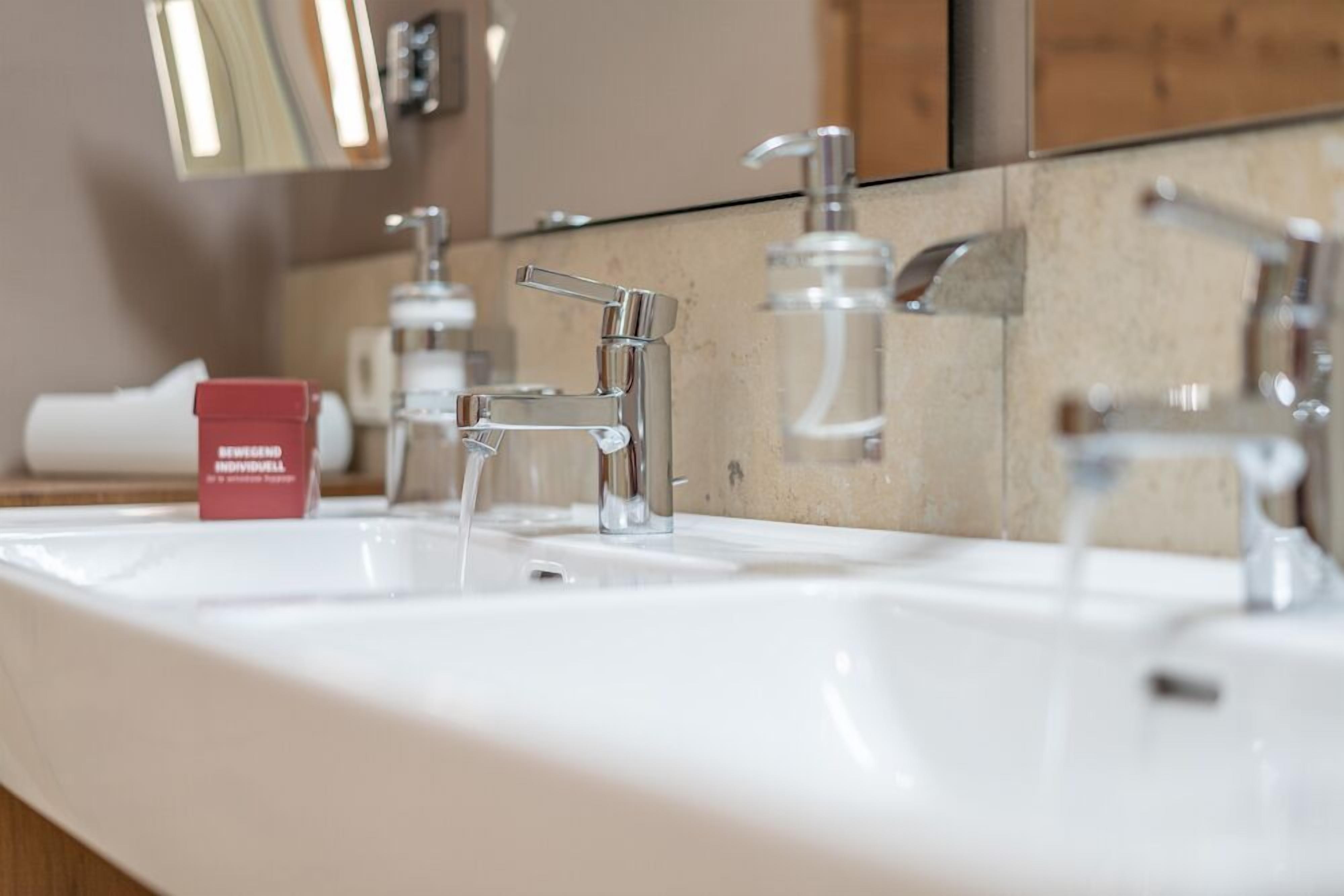 Un baño con lavamanos blanco, dos llaves y un espejo.