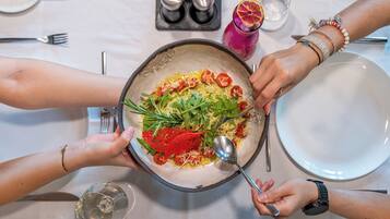 Una mesa de comedor con un bol grande de ensalada, varios utensilios y un vaso de agua.