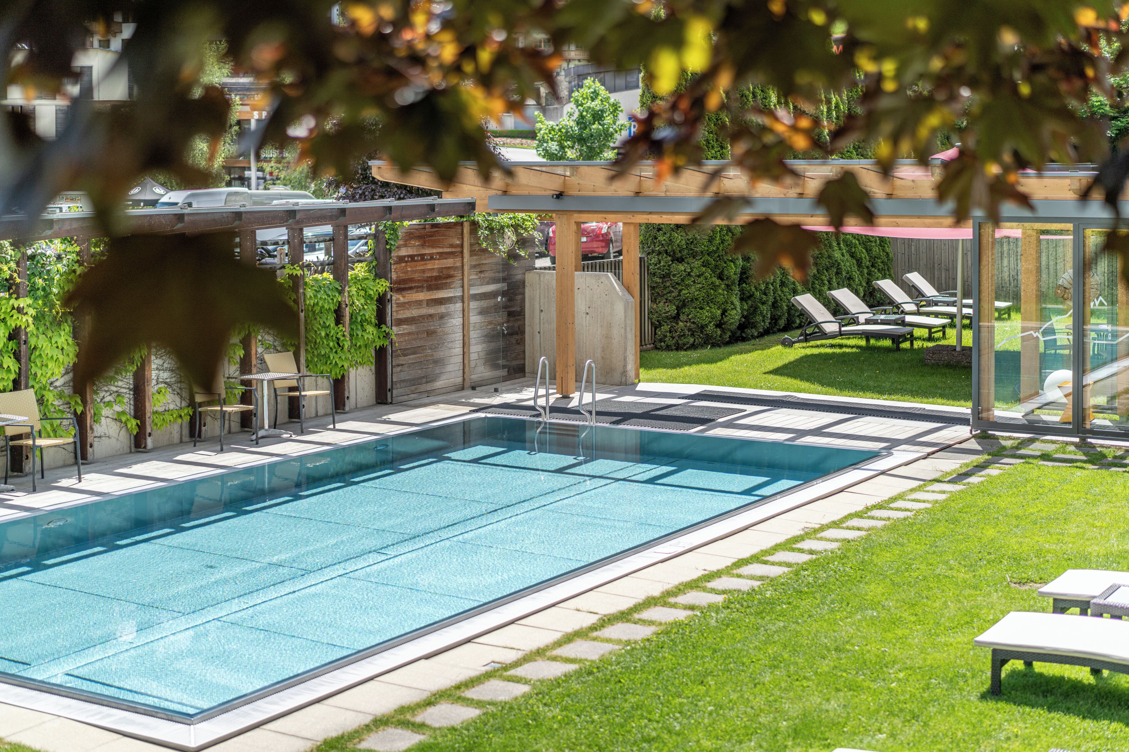 Uma piscina retangular com superfície azul límpida, rodeada por um deck ladrilhado e uma área gramada com espreguiçadeiras.