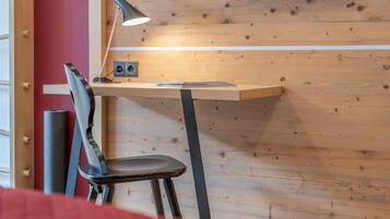 A wooden desk with a lamp, a chair, and a red wall.