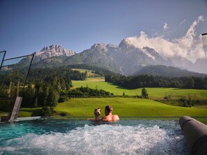 A hot tub with a view of mountains and a green landscape. - Salzburger Hof (Leogang)