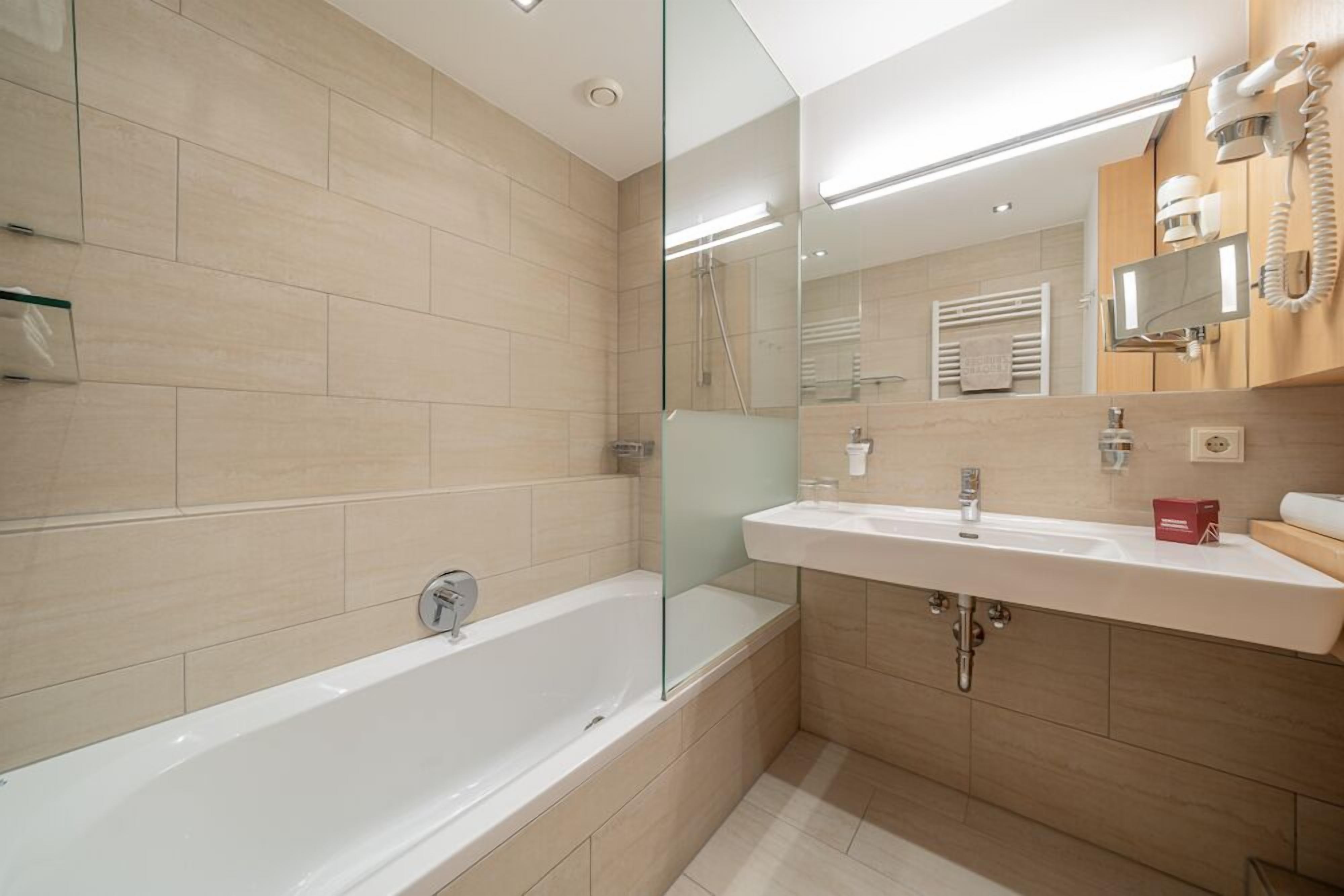 Ein modernes Badezimmer mit einer Duschkabine, einer weißen Badewanne und einem Waschtisch mit Spiegel und Waschbecken.