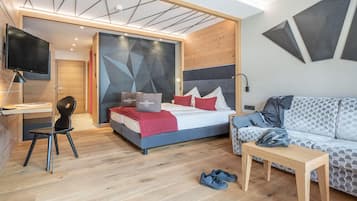 Quarto de hotel moderno com cama, escrivaninha, poltrona, sofá e televisão.