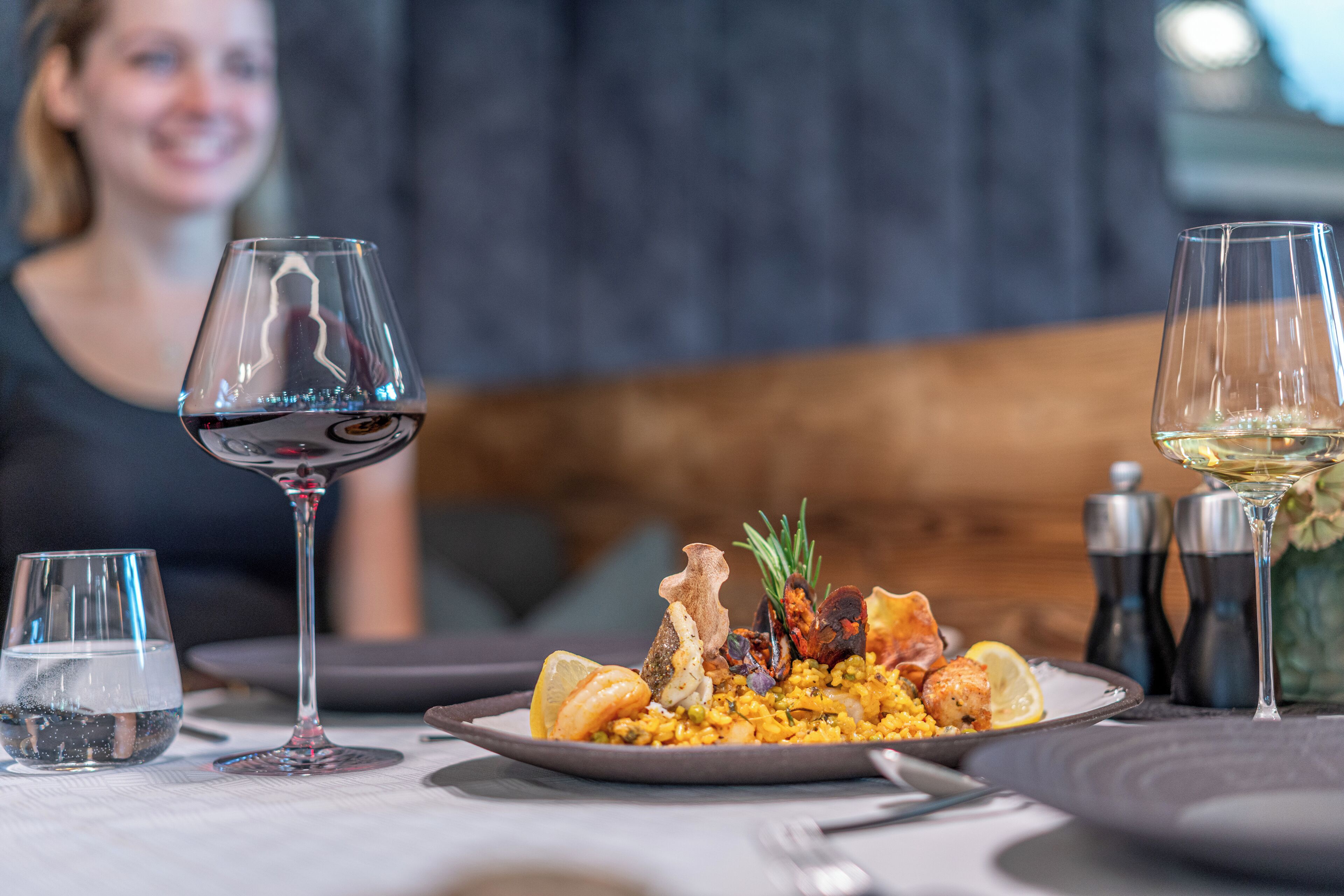 A dining table with a plate of seafood and rice, two wine glasses, and salt and pepper shakers.