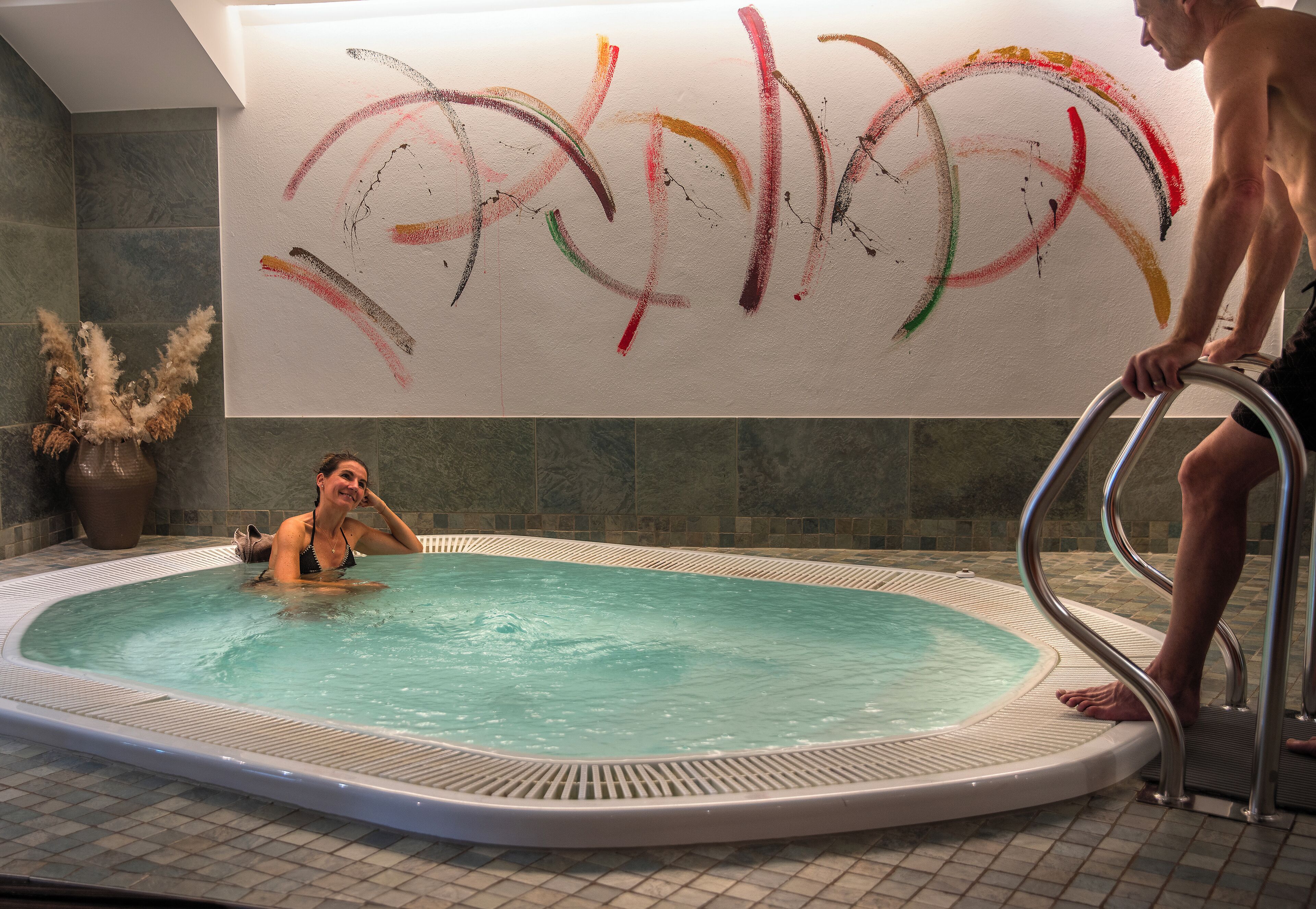 A swimming pool with a tiled floor and a wall with abstract art.