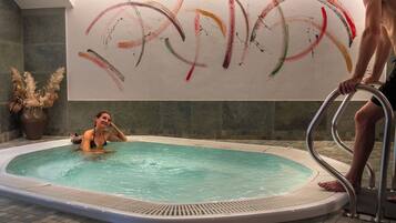 A swimming pool with a tiled floor and a wall with abstract art.