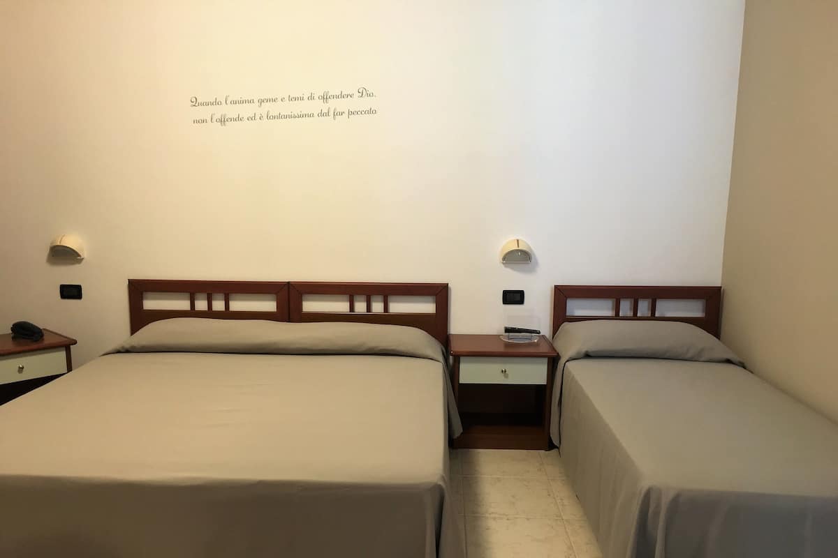 Une chambre d’hôtel avec deux lits simples, des têtes de lit en bois, des tables de chevet avec des lampes et un luminaire fixé au mur.