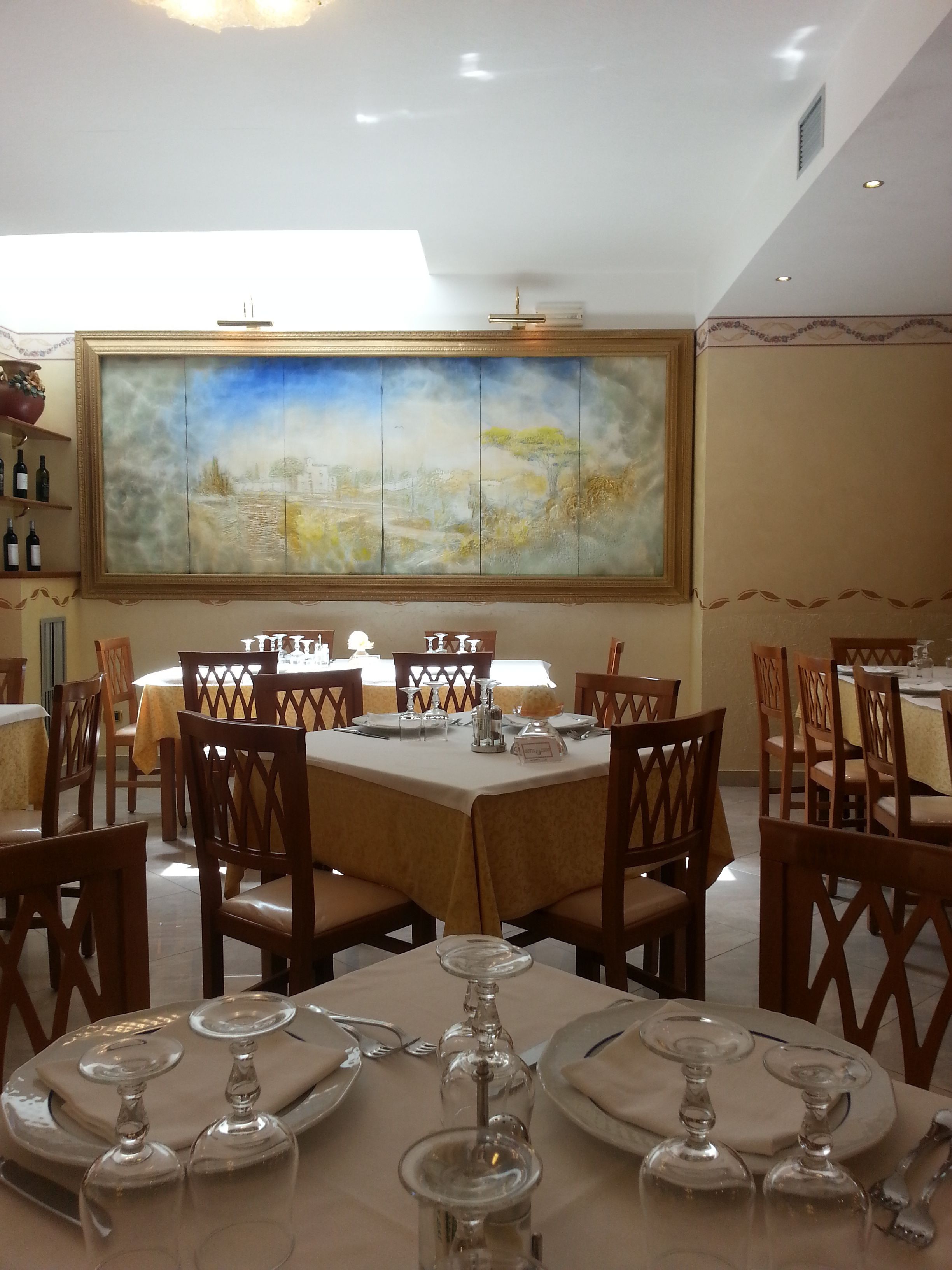 A dining area with tables set for a meal, chairs, and a large painting on the wall.