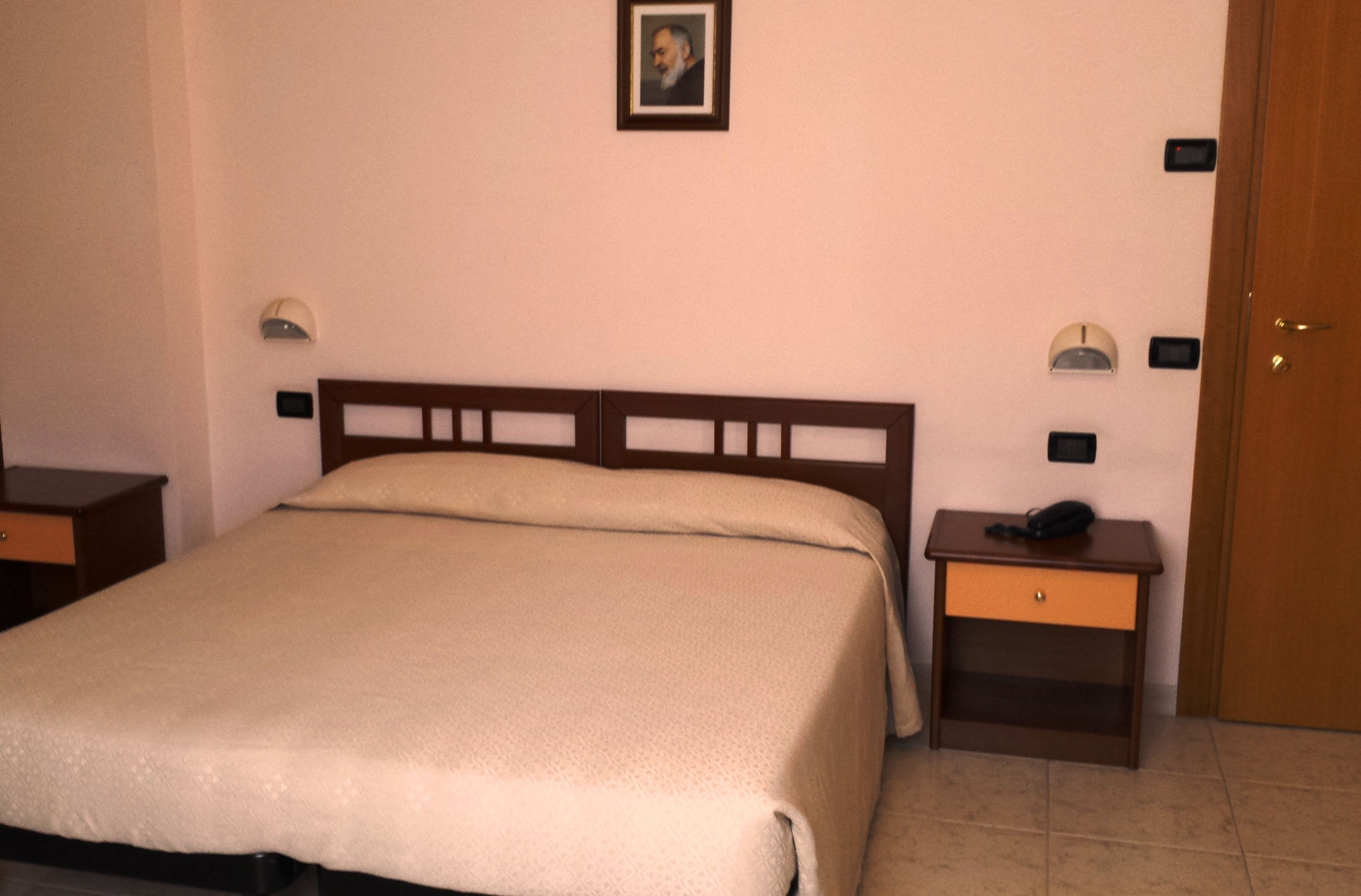 Un dormitorio con cama, mesitas de noche, una puerta y una lámpara fijada a la pared.