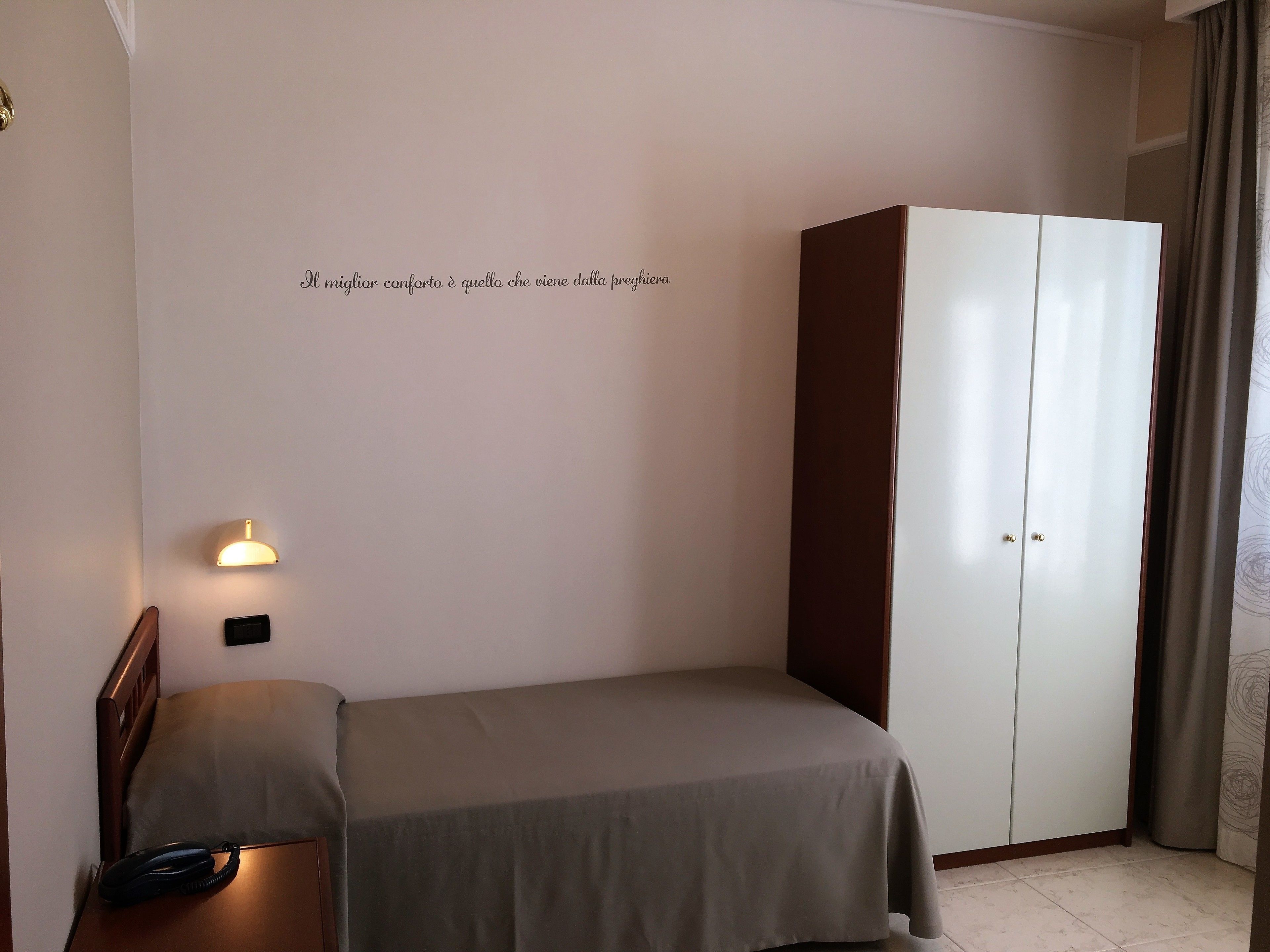 Una camera da letto con un letto, un armadio, una lampada sul comodino e una luce a parete.