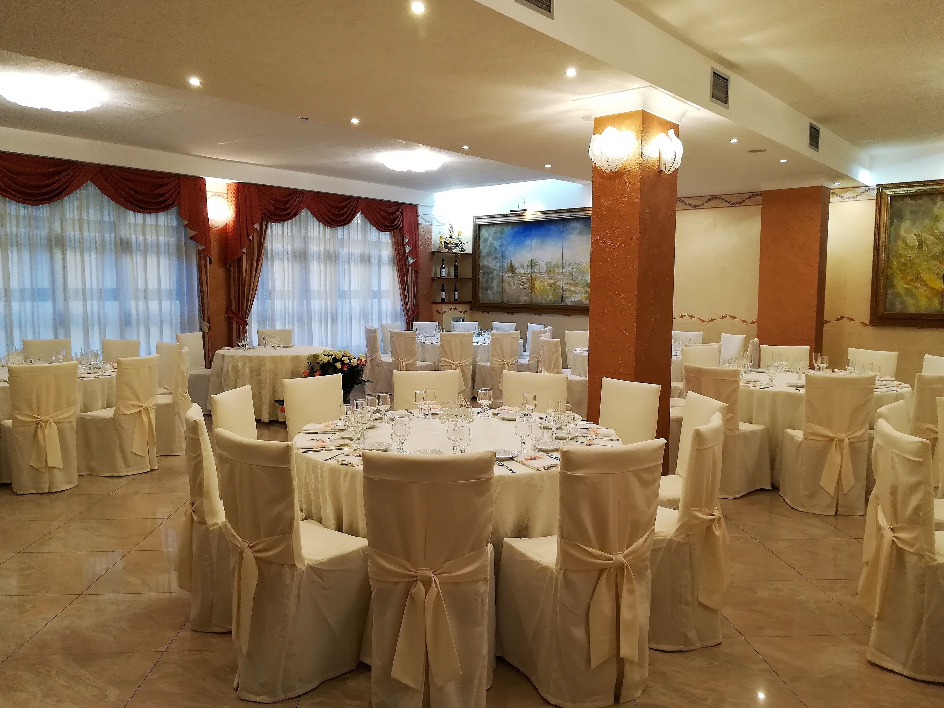 A banquet hall with round tables, white chairs, and red curtains.