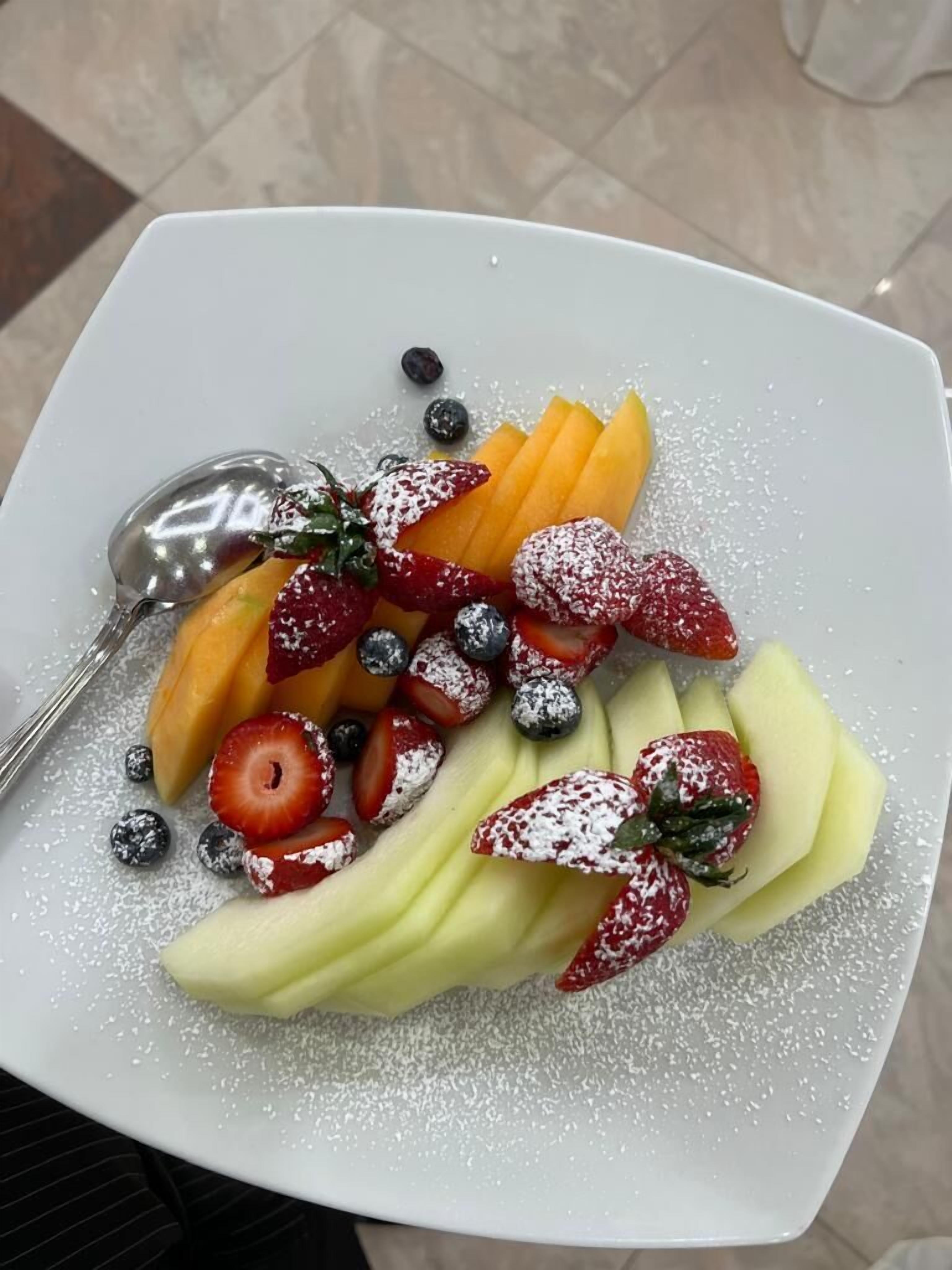 A white plate with a variety of fruits including strawberries, blueberries, and cantaloupe, garnished with powdered sugar.